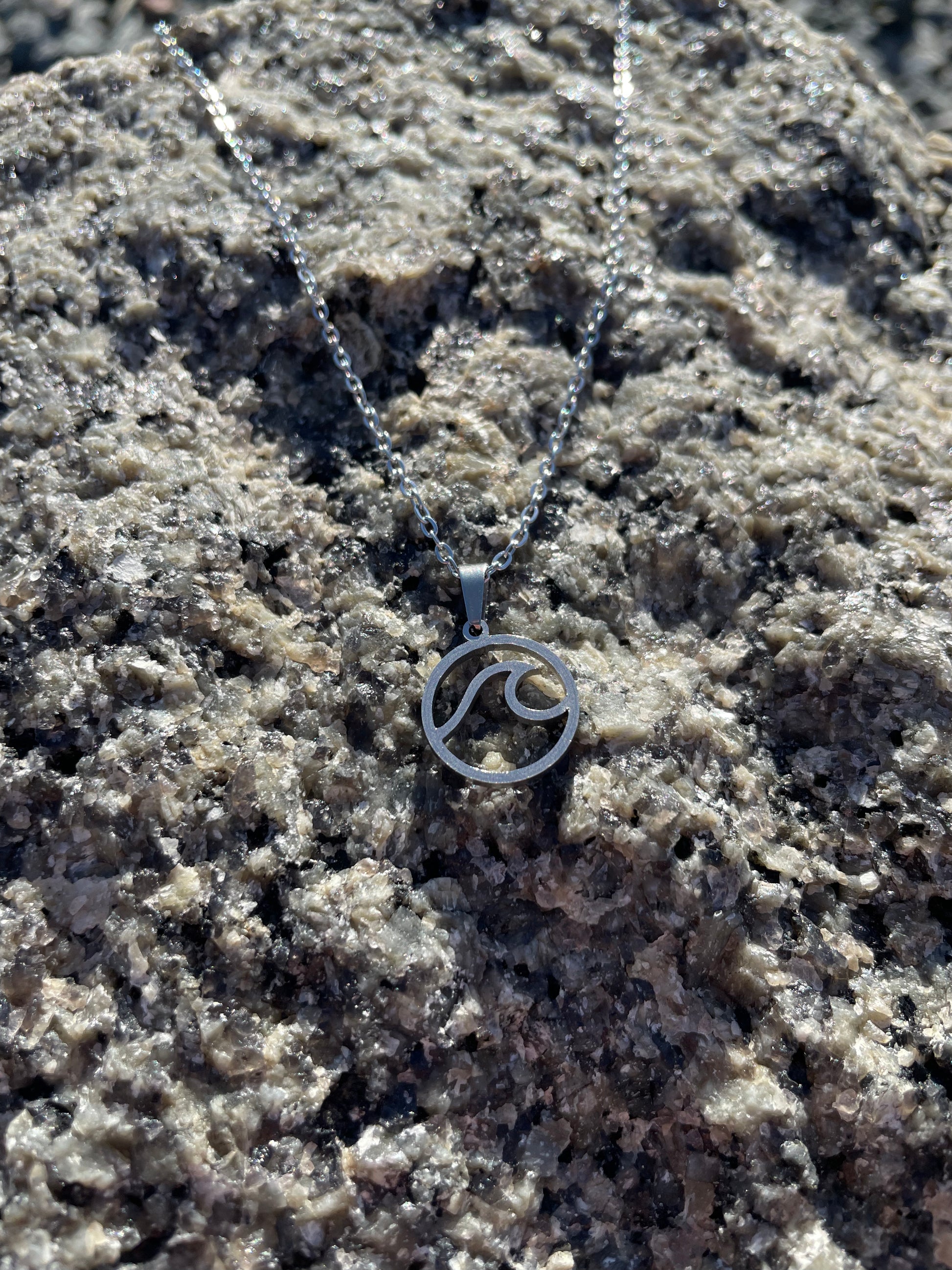 Stainless steel wave necklace laying on a rock